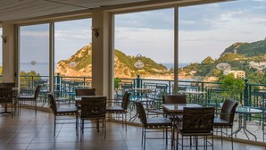 A terrace with outdoor seating, large windows, and a view of a mountainous landscape. - Paleokastritsa Palace (Corfu)