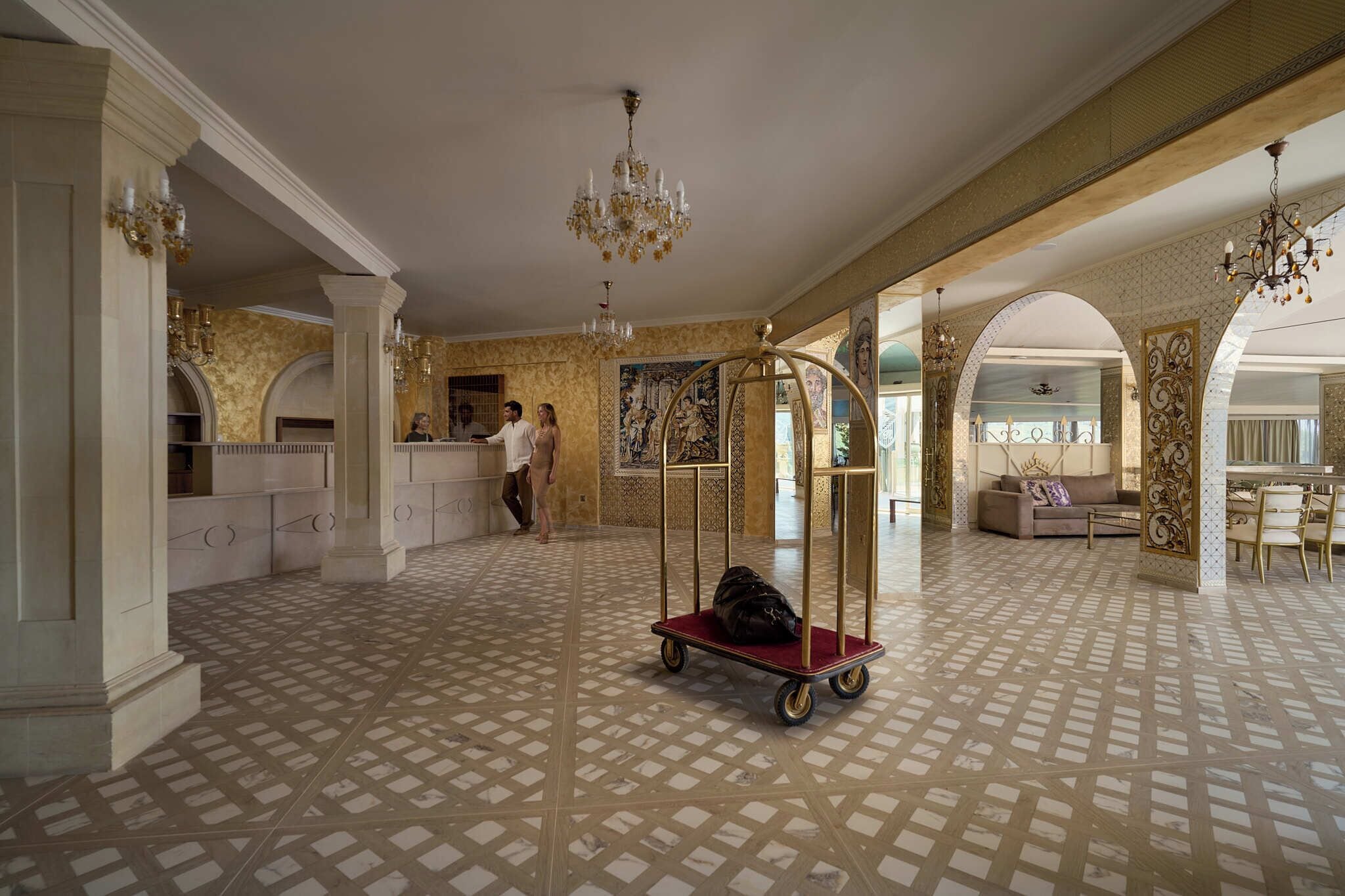 Un hall d’hôtel spacieux, doté d’un sol à motifs, d’un lustre central et d’un comptoir d’accueil.
