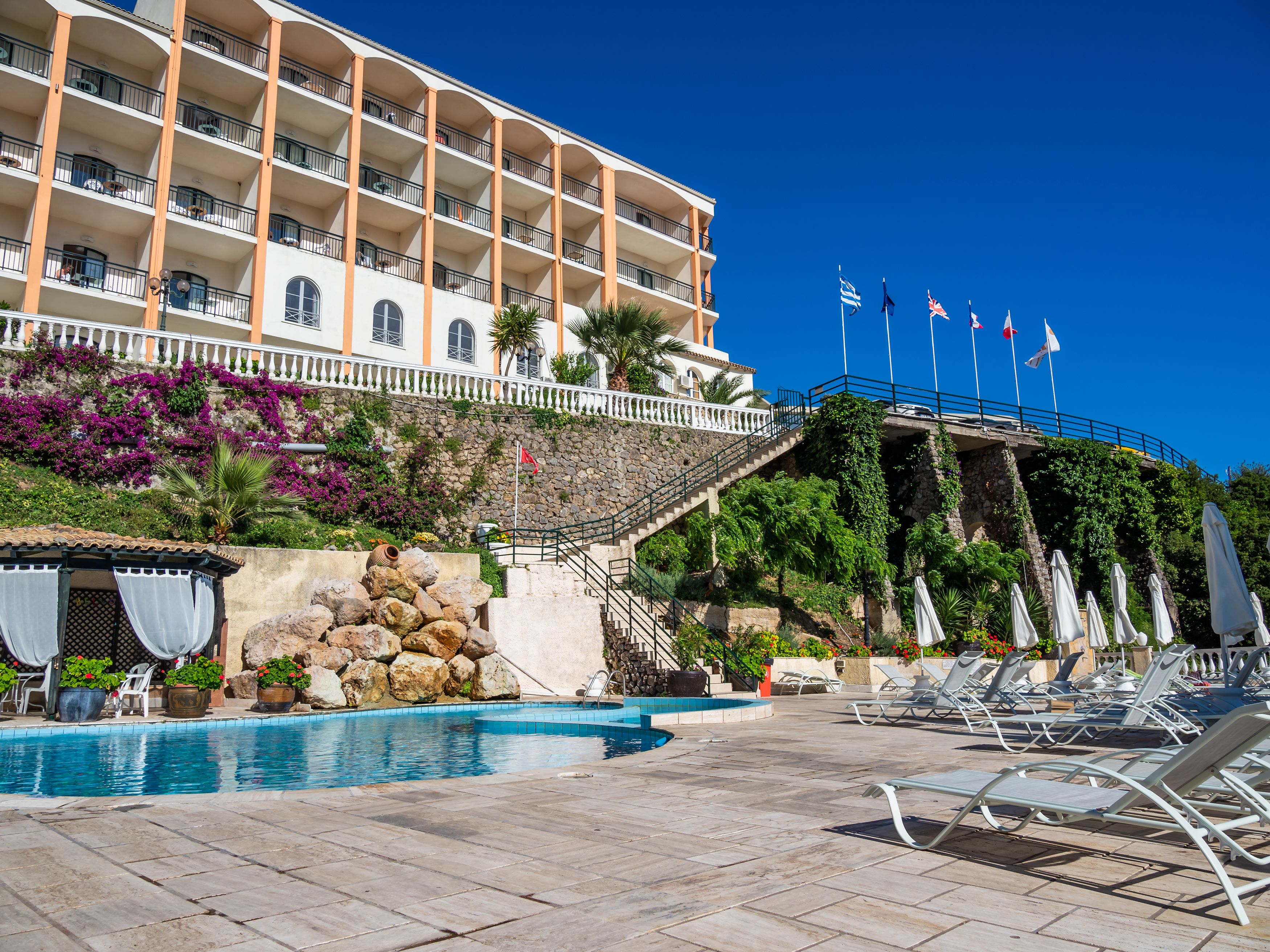 A hotel with a swimming pool, outdoor lounge chairs, and a staircase leading to the upper floors.