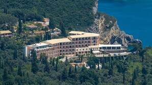 A large hotel with multiple floors, surrounded by dense forest and a rocky coastline. - Paleokastritsa Palace (Corfu)