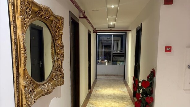 A hallway with a marble floor, a large ornate mirror, and a potted plant with red flowers. - Hotel Idea Inn (Agra)