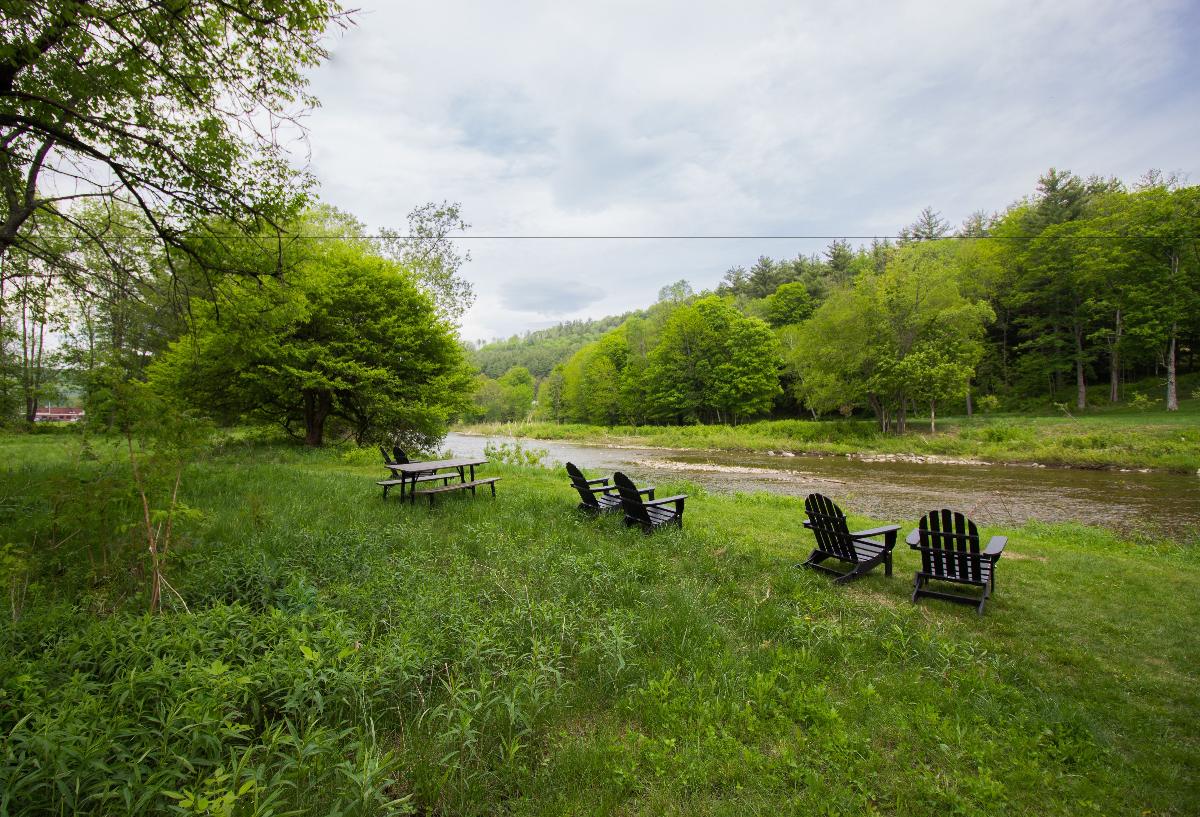 A riverside picnic area with benches and Adirondack chairs.