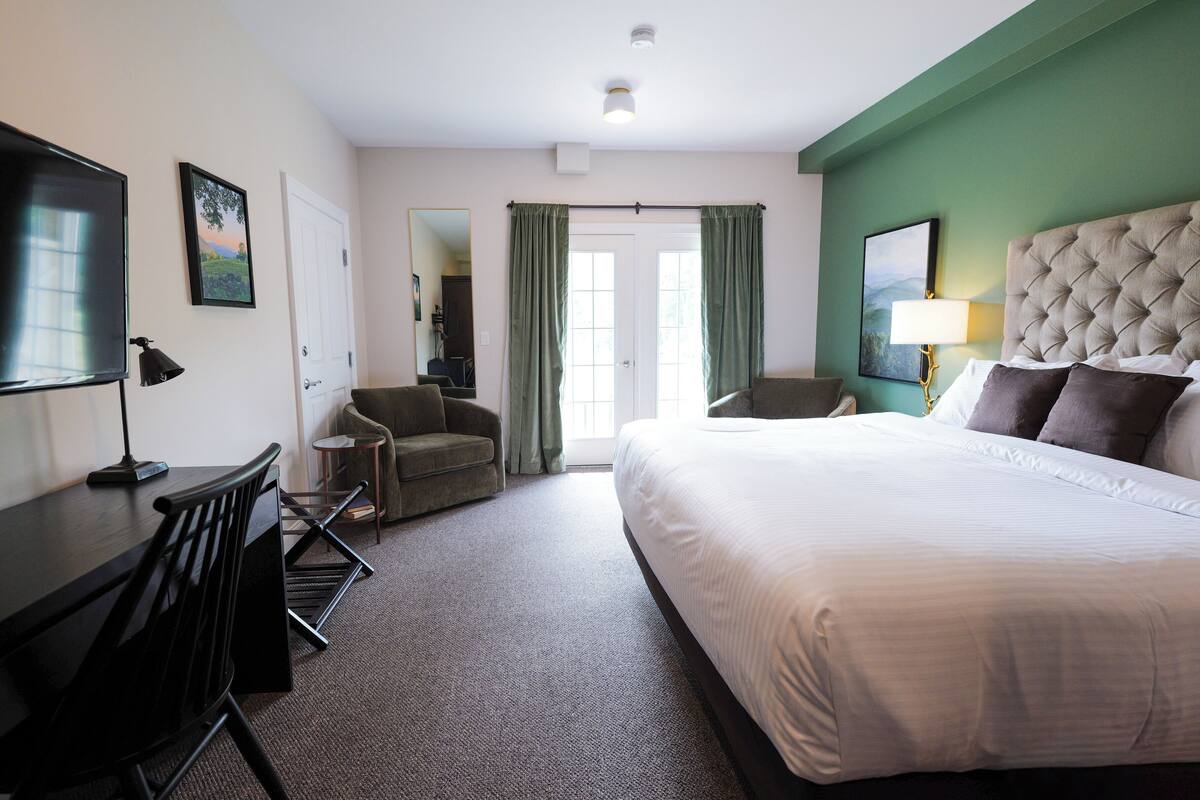 Habitación de hotel con una cama grande, un escritorio con silla, televisión y pared verde.