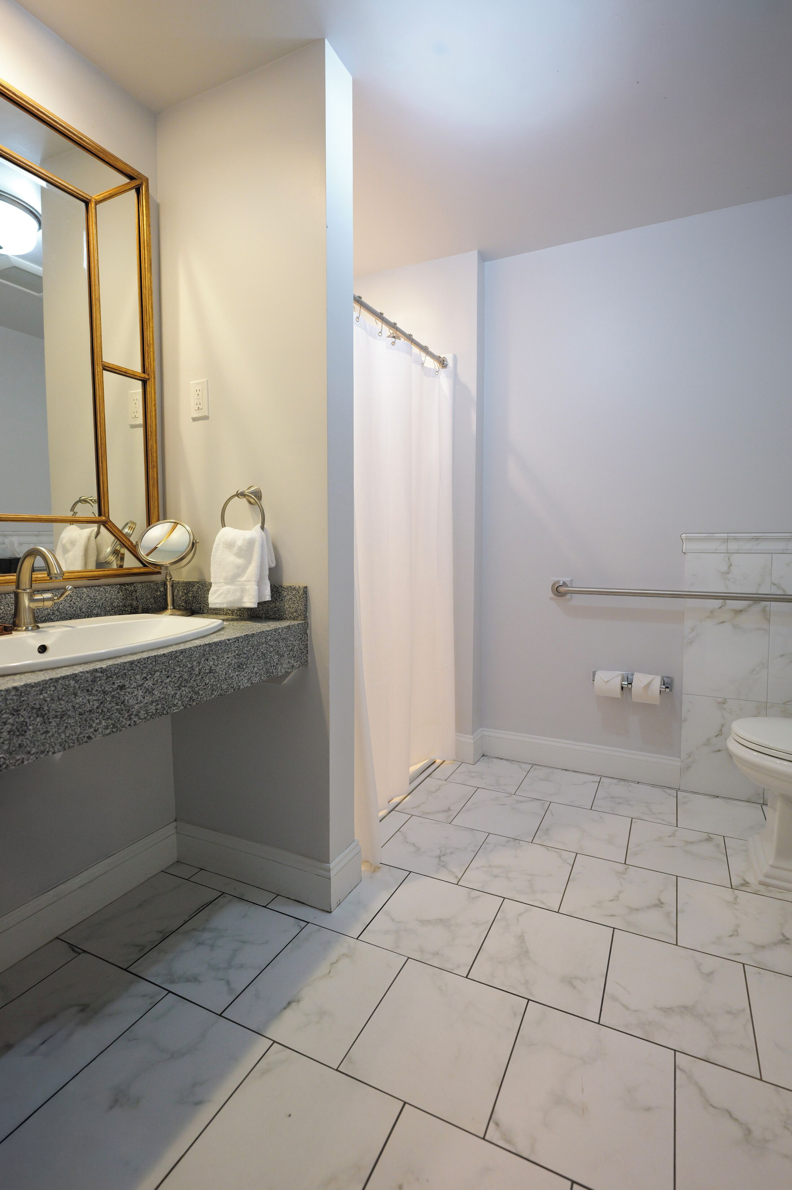A bathroom with a marble floor, a sink with a gold faucet, a large mirror, and a shower area with a glass door.