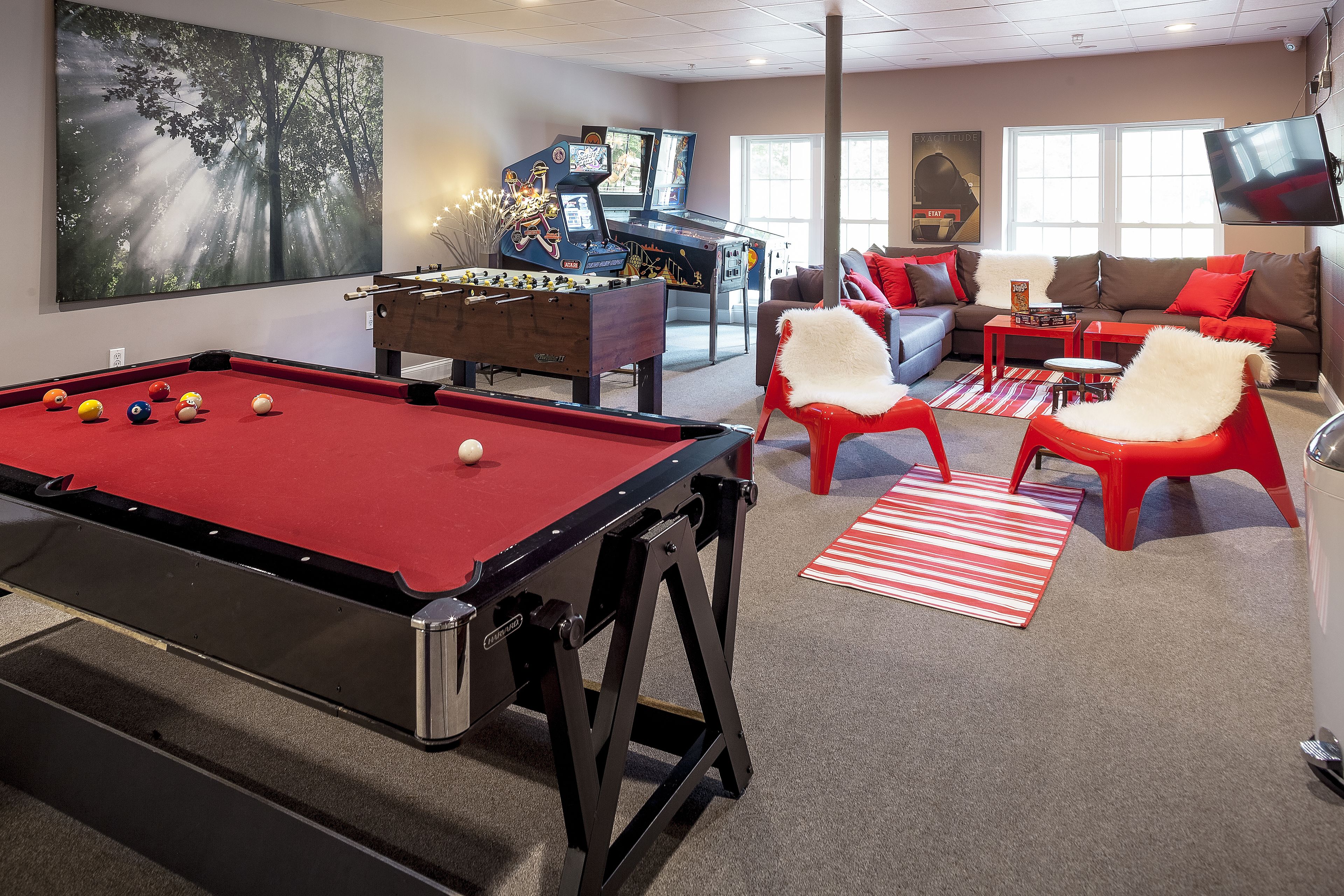 A pool table, a foosball table, a sofa, and a television in a living room.