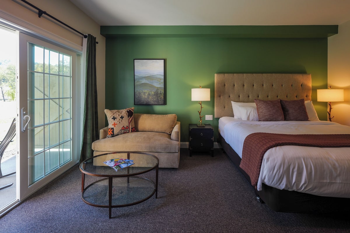 Una habitación de hotel con cama, sofá, mesa de centro y un cuadro en la pared.