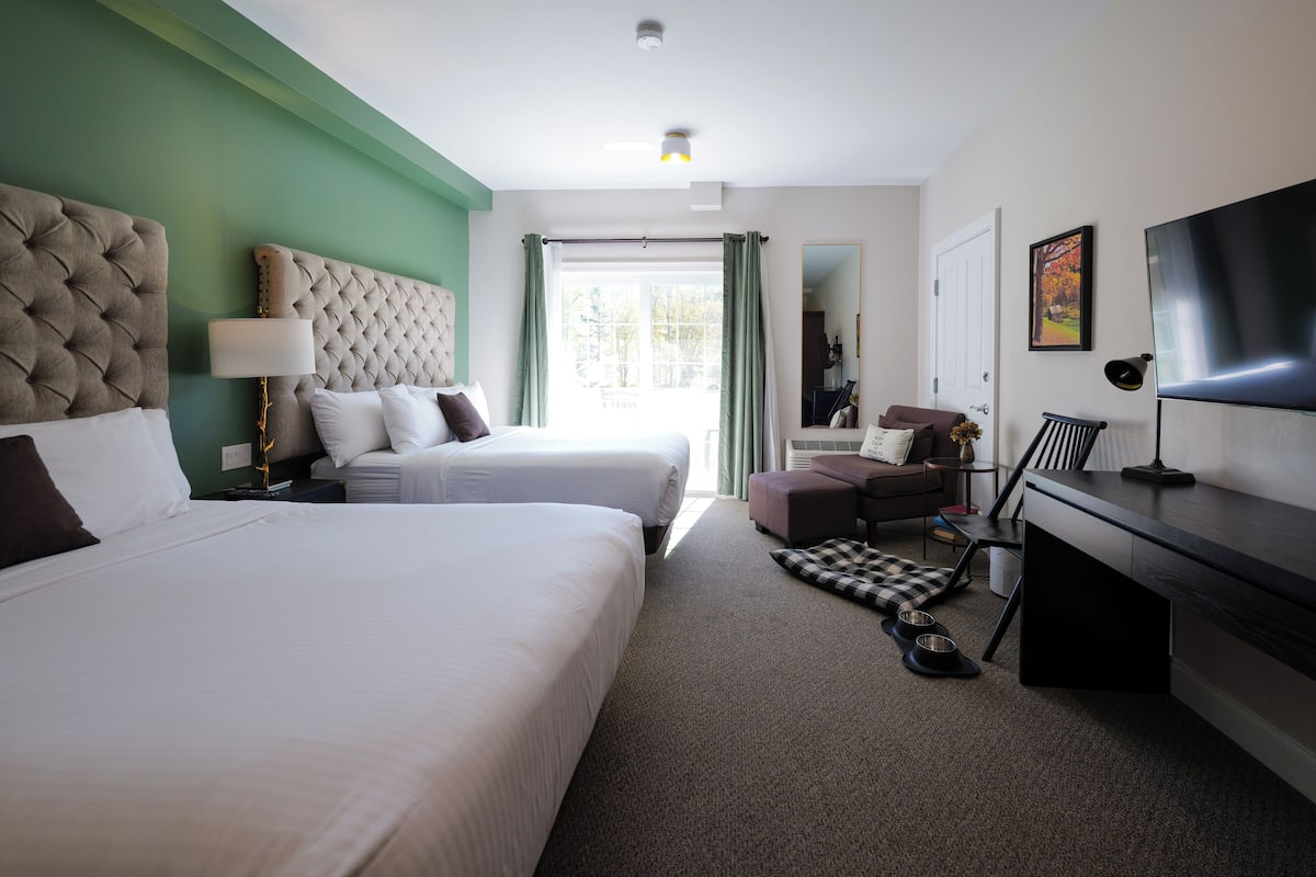 Habitación de hotel con dos camas, un escritorio, televisor y vistas al exterior.