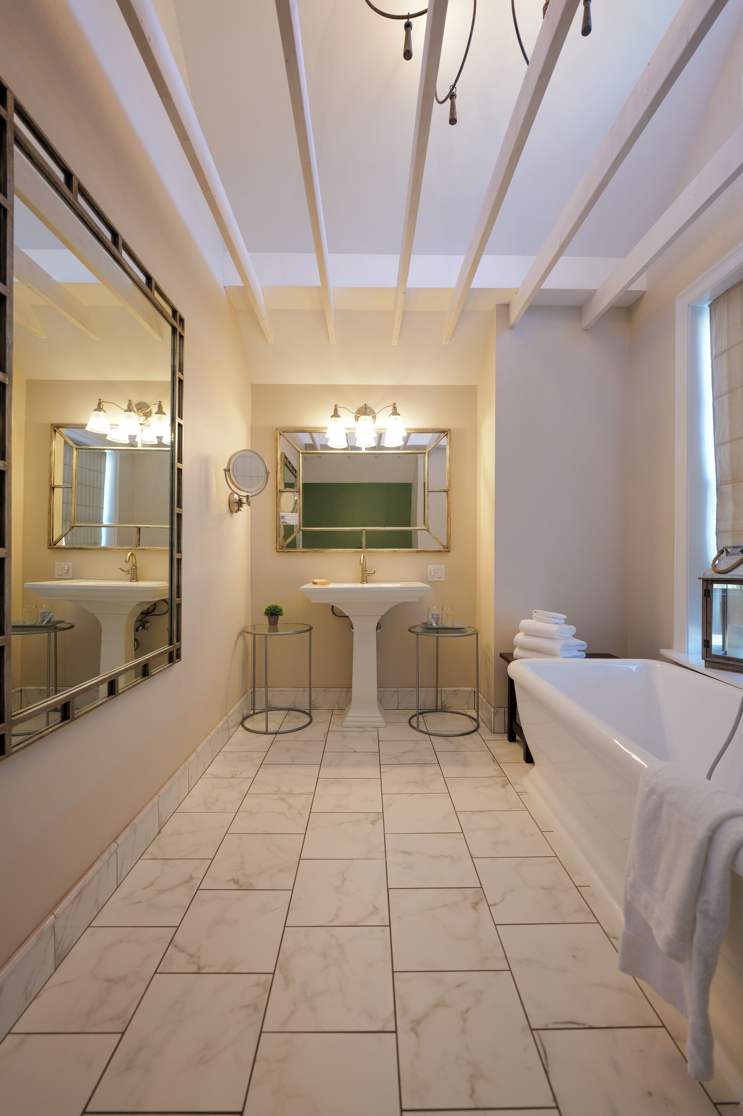 Un baño con un espejo grande, un lavamanos, una bañera y un techo con vigas a la vista.
