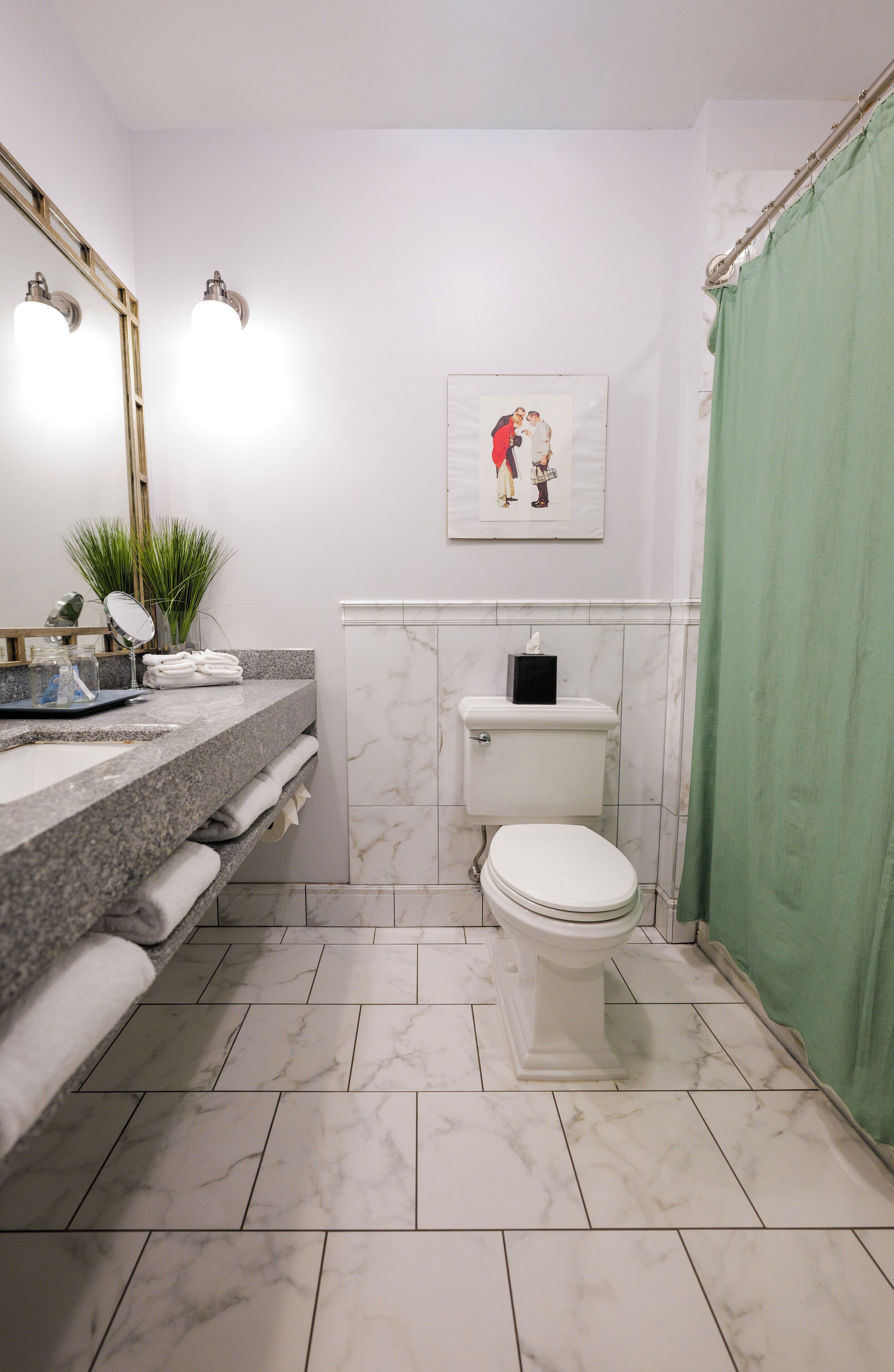 Een badkamer met een marmeren vloer, een toilet, een wastafel met spiegel en een fotokader aan de muur.