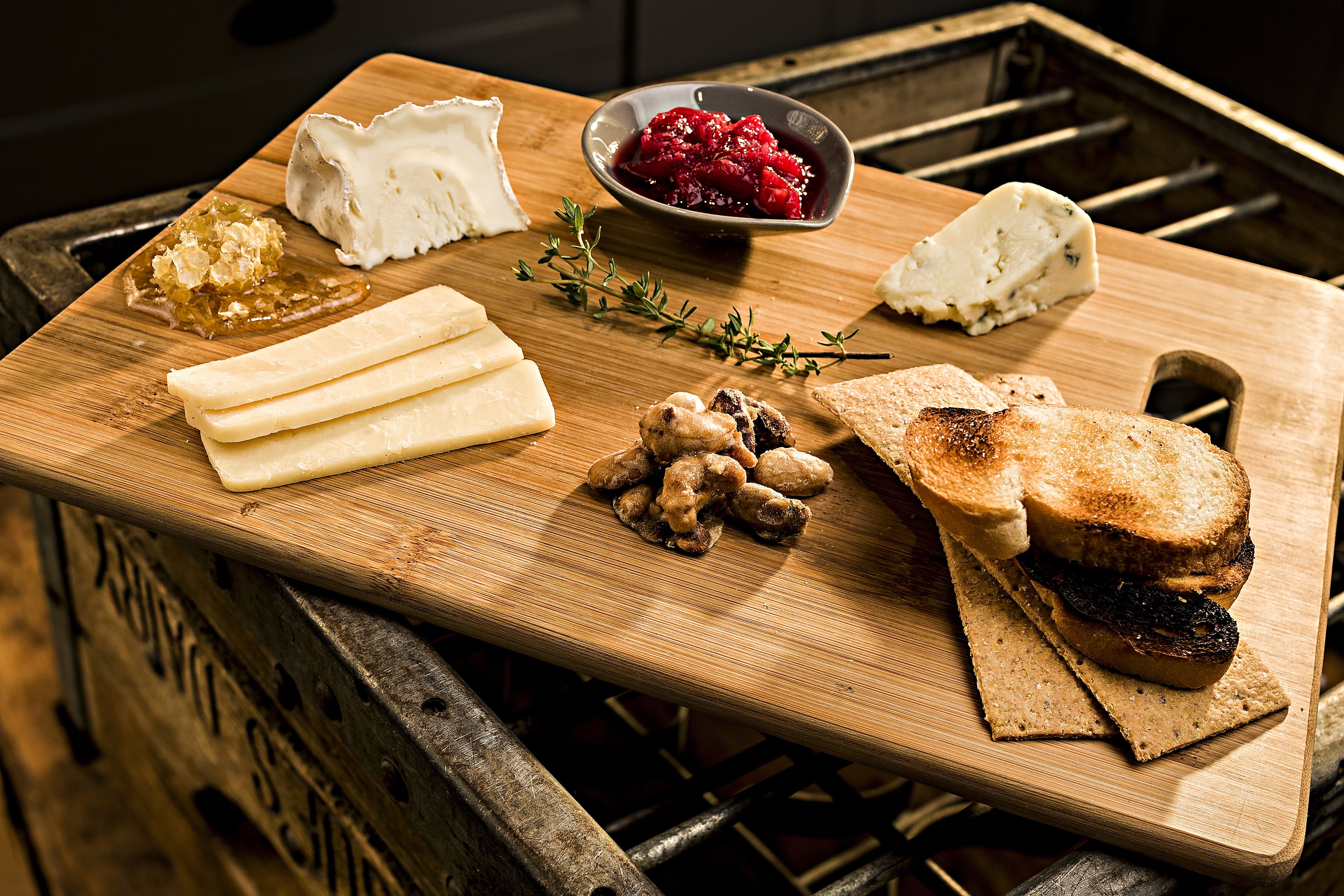 A wooden cutting board with various cheeses, a bowl of berries, and some bread.