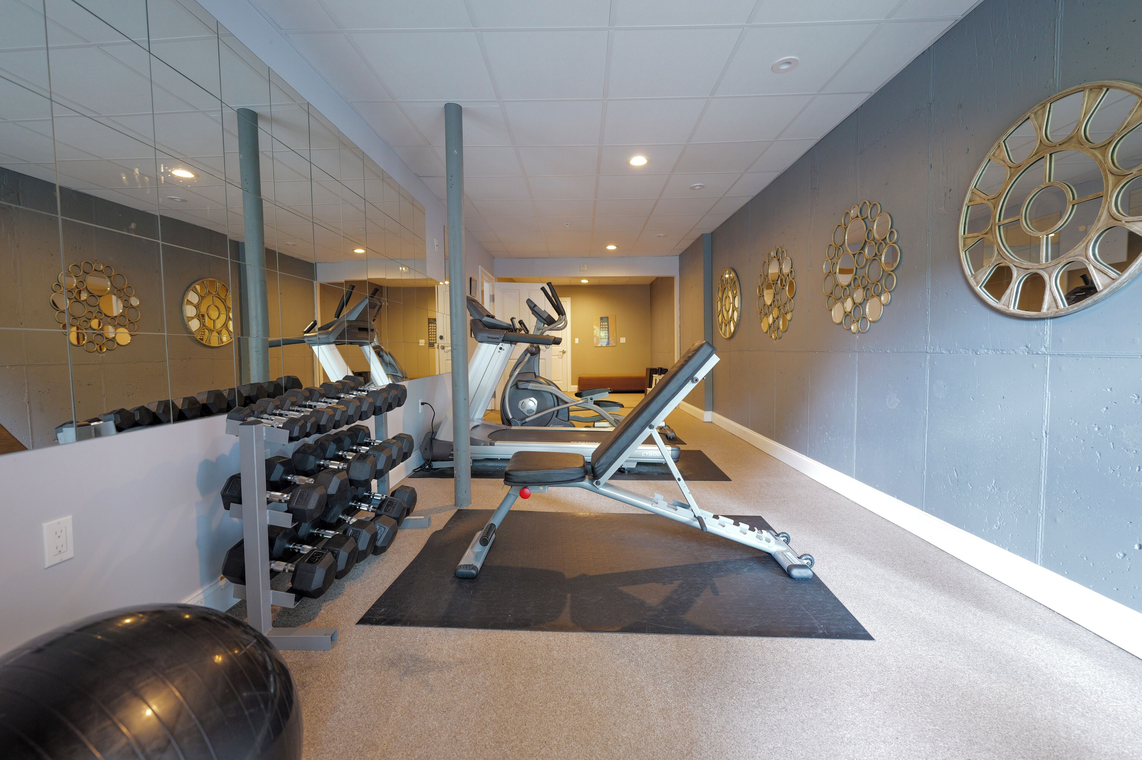 A gym with exercise equipment, a mirrored wall, and a patterned wall design.