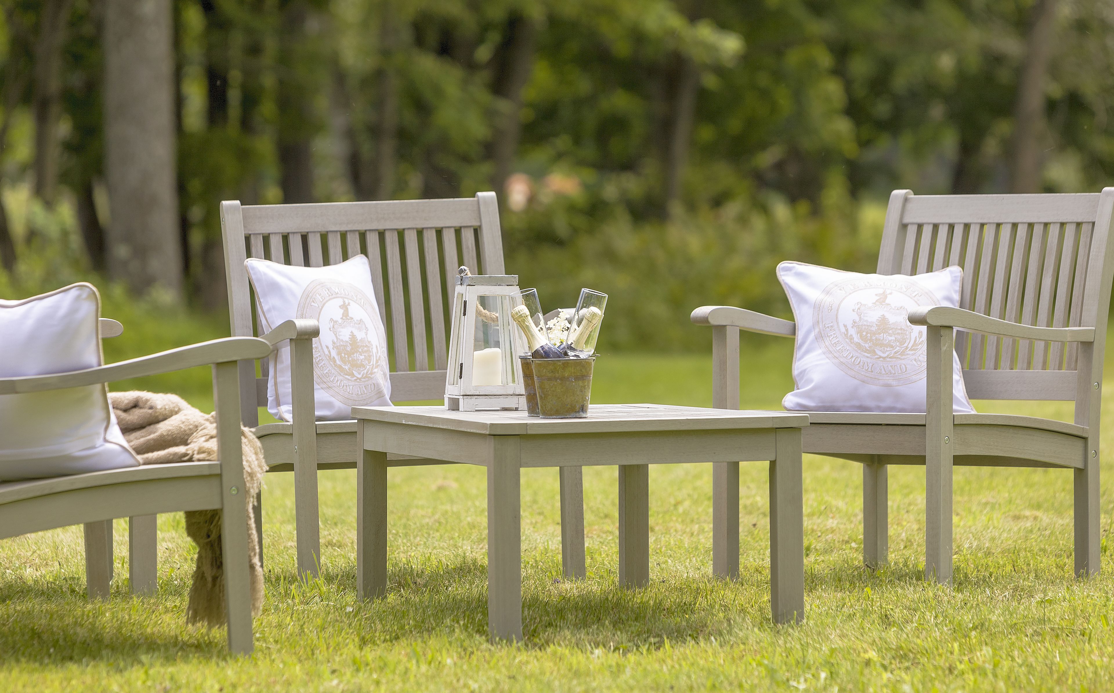 Two wooden chairs with white cushions and a small table with a bottle holder in between.