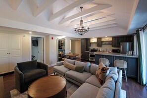 A modern living room with a sofa, chairs, and a round coffee table. There is a kitchen area with a refrigerator, stove, and cabinets.