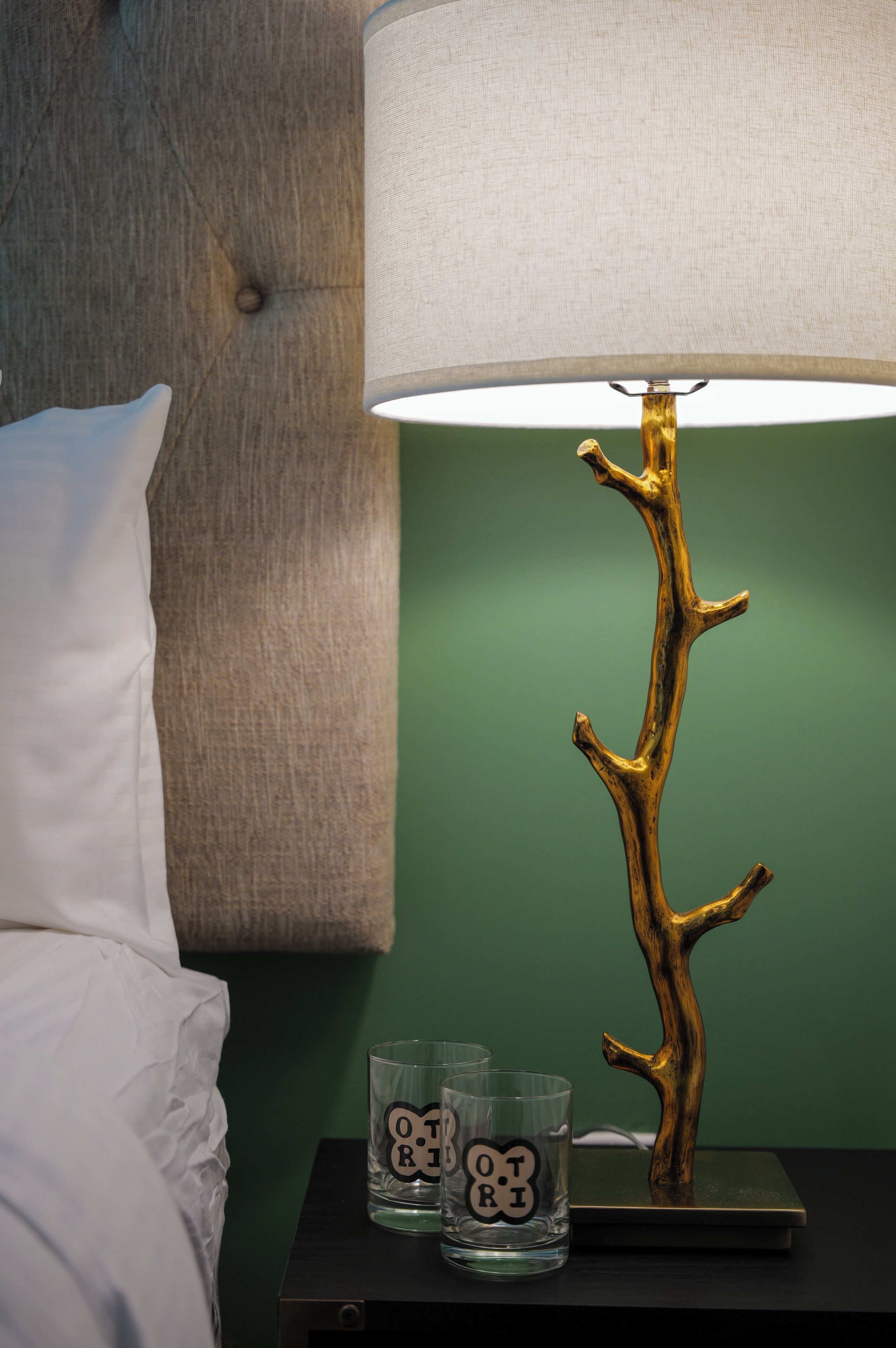 A bed with a grey headboard, a bedside table with a lamp, and two glasses with 'OTORI' text.