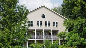 A two-story house with a balcony, surrounded by lush greenery and a pond. - On The River Inn (Woodstock)
