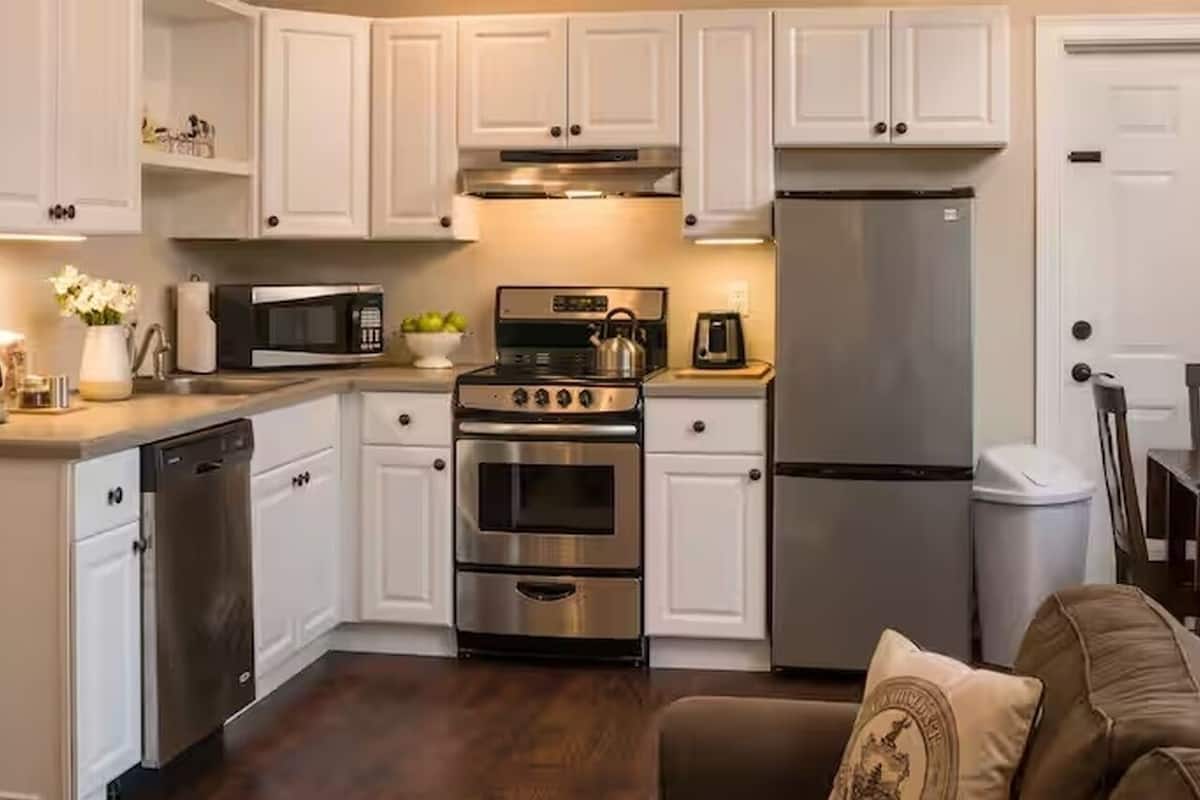 Una cocina con armarios blancos, un refrigerador de acero inoxidable, un lavavajillas, una estufa y un microondas.