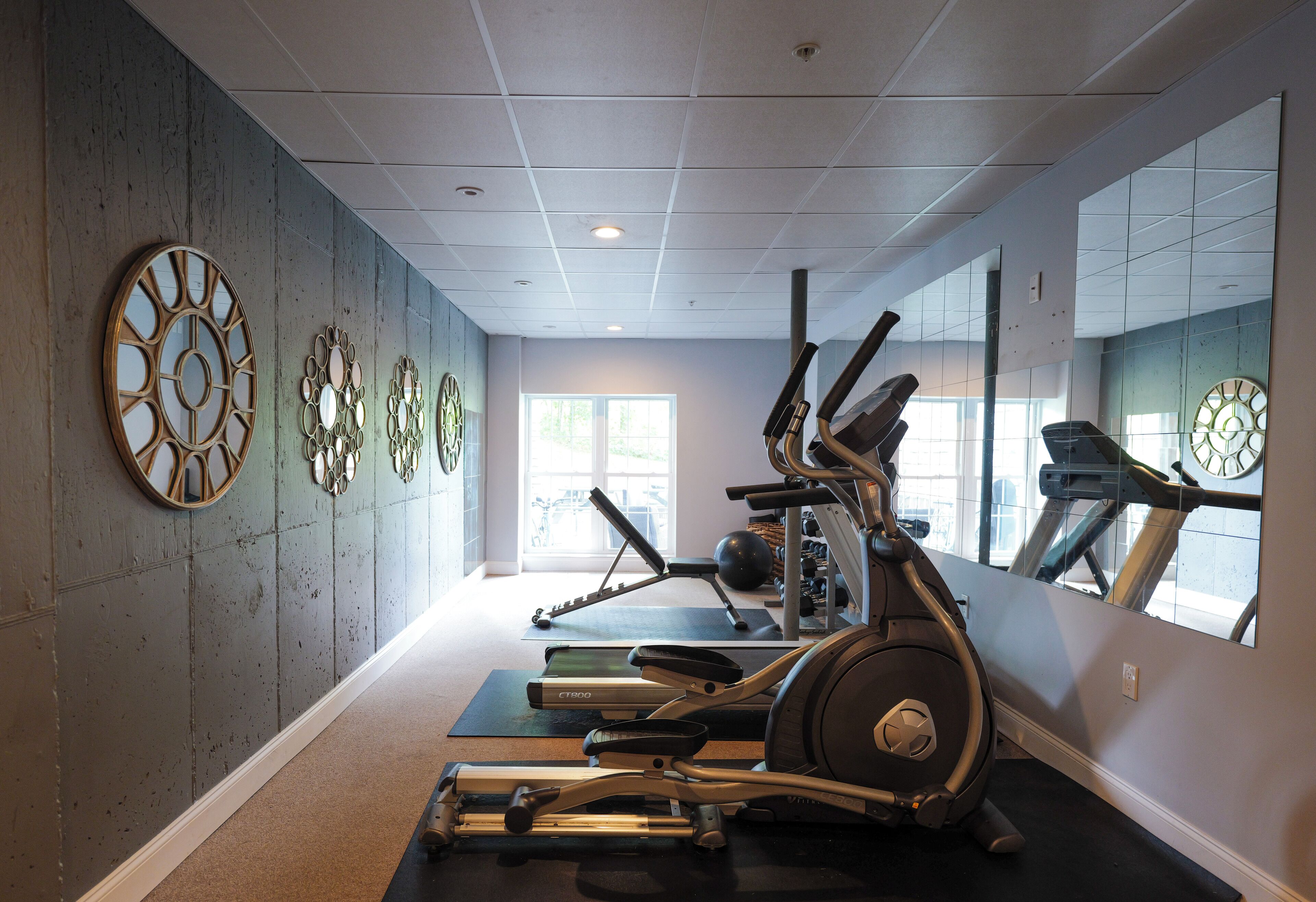 Ein Fitnessraum mit Trainingsgeräten, einem großen Spiegel und dekorativen Wanduhren.