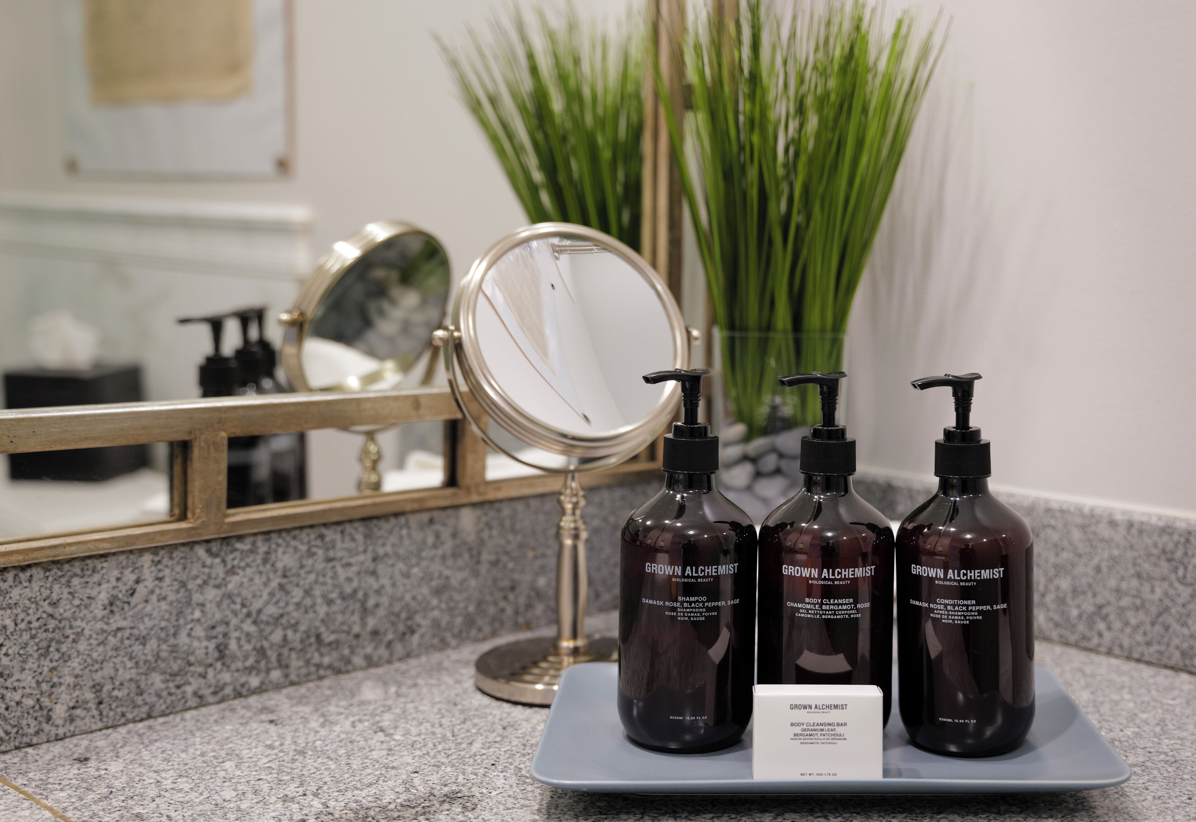Un tocador de baño con espejo, lavamanos y tres botellas de productos 'Grown Alchemist'.