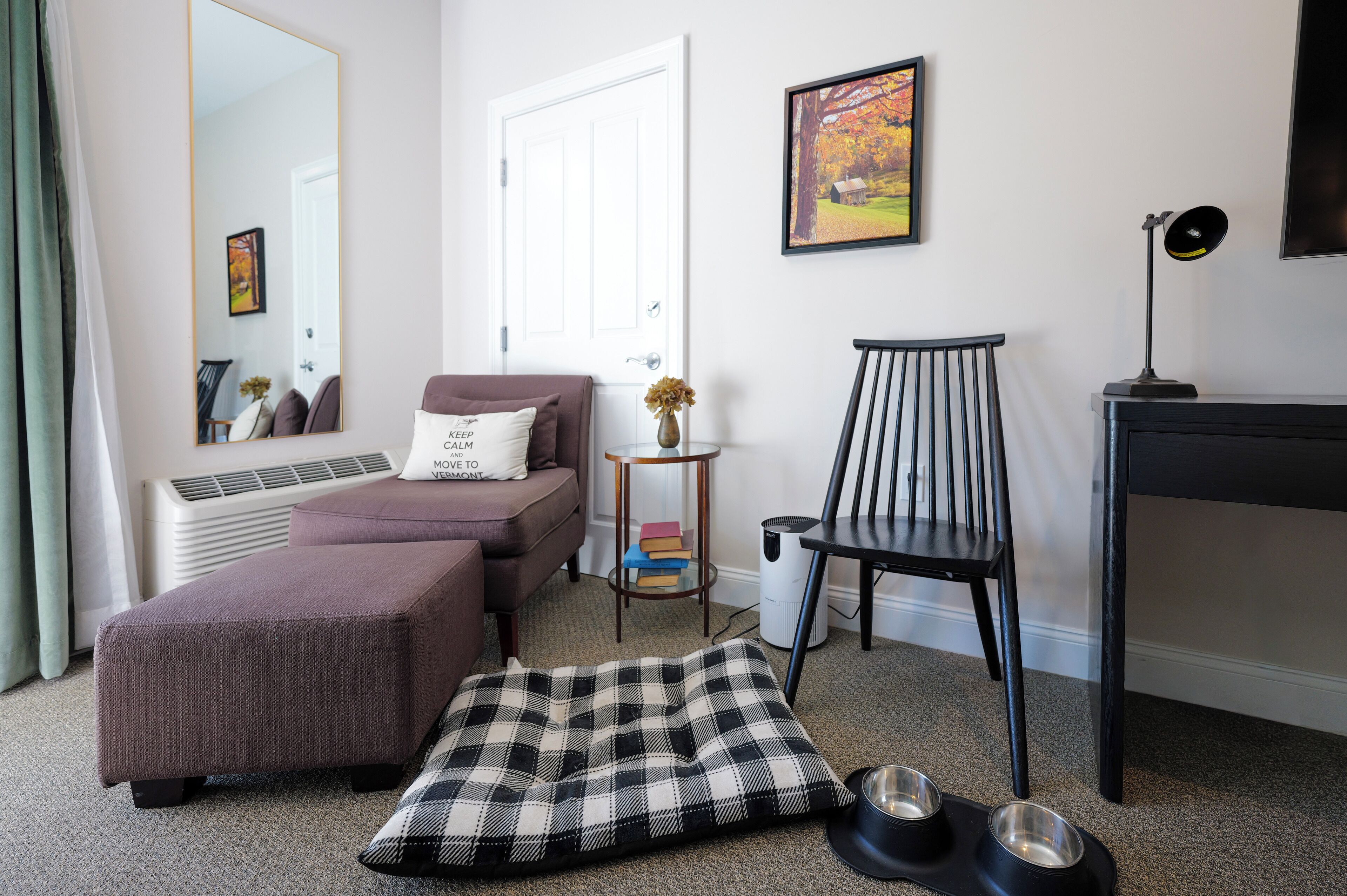 A modern living room with a sofa, ottoman, chair, and a small table with a lamp.
