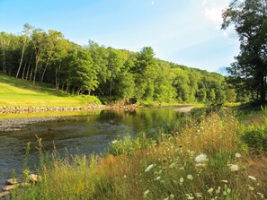 A river with a stone embankment, surrounded by lush greenery and trees. - On The River Inn (Woodstock)