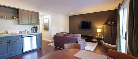 A modern living room with a sofa, a dining table, and a kitchen area with cabinets and a dishwasher.