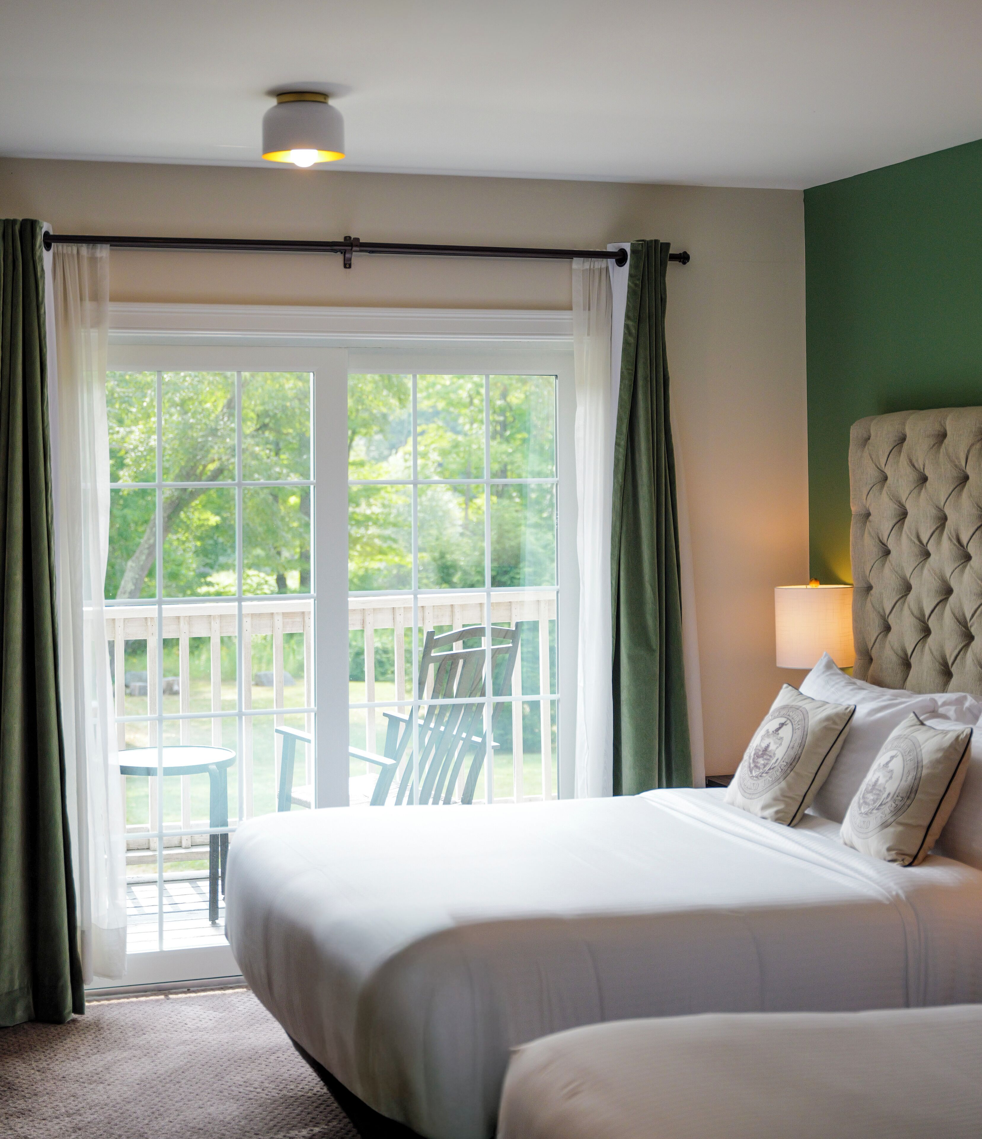 A hotel room with a large bed, a view of the outdoors, and a balcony with chairs.