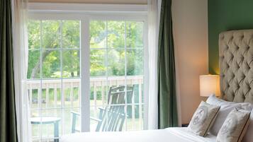 A hotel room with a large bed, a view of the outdoors, and a balcony with chairs.