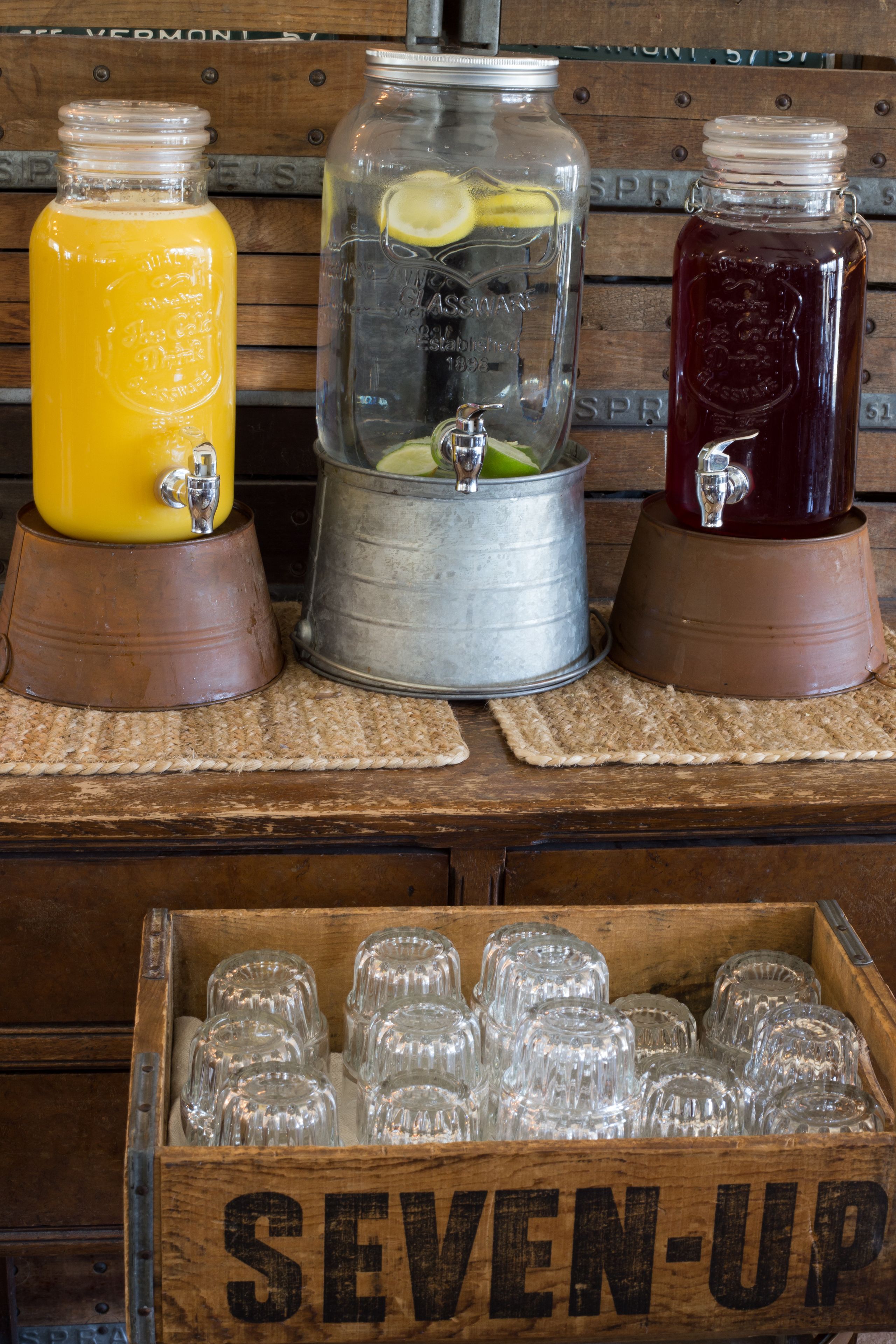 A wooden bar area with three drink dispensers and a crate of glasses labeled "SEVEN-UP".