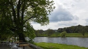 A riverside picnic area with tables and chairs, surrounded by a stone wall and lush greenery. - The Kenbridge Hotel (Castle Douglas)