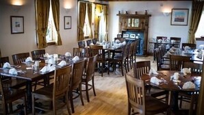 A dining area with wooden tables and chairs, a fireplace, and framed pictures on the walls. - The Kenbridge Hotel (Castle Douglas)