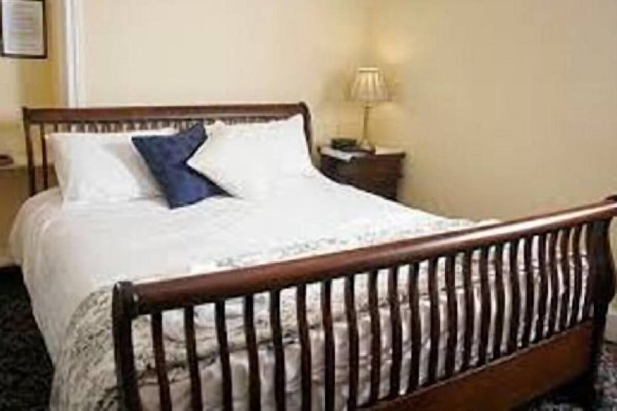 A bed with a wooden headboard, a nightstand with a lamp, and a framed certificate on the wall.