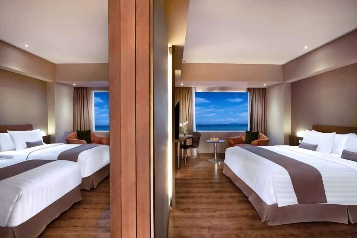 Une chambre d’hôtel avec deux lits, un plancher en bois, une vue sur la mer et un coin repas.