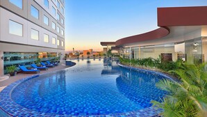 A modern hotel with a large pool, lounge chairs, and a view of the city skyline. - Aston Kupang Hotel & Convention Center (Kupang)