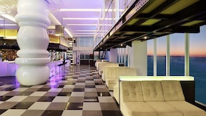 A modern hotel lobby with a checkered floor, a large white sculpture, seating areas, and a view of the sea through large windows. - Aston Kupang Hotel & Convention Center (Kupang)