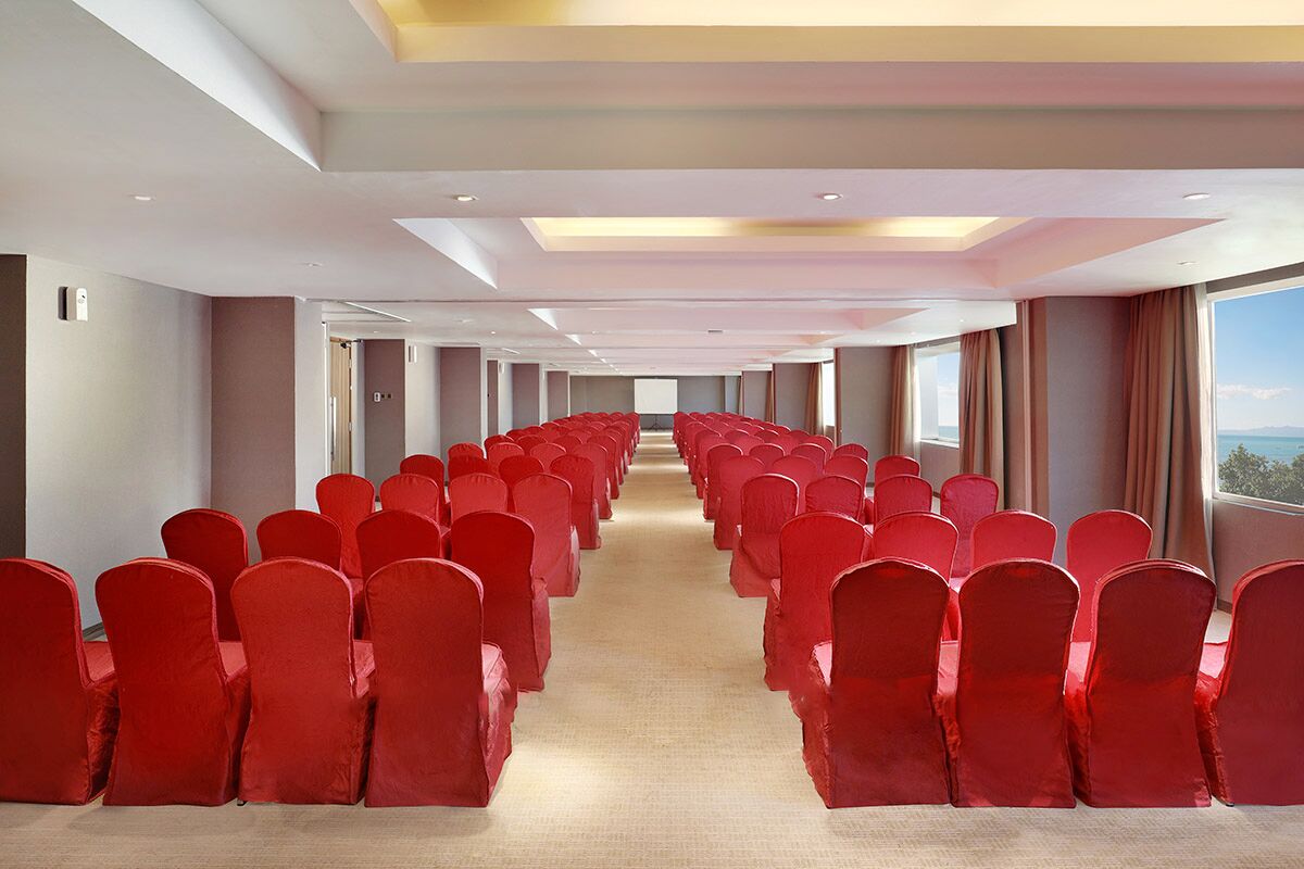 A conference room with rows of red chairs and a carpeted floor.