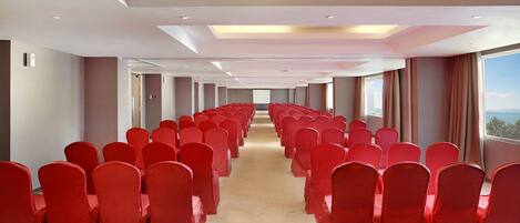 A conference room with rows of red chairs and a carpeted floor.