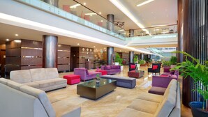 A spacious lobby with multiple seating areas, a staircase, and a high ceiling with modern lighting. - Aston Kupang Hotel & Convention Center (Kupang)