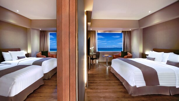 A hotel room with two beds, a small table, a chair, and a view of the sky through a large window. - Aston Kupang Hotel & Convention Center (Kupang)