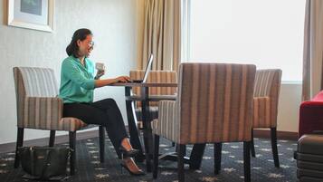 A person sitting at a table with a laptop and a cup, in a room with striped chairs and a carpeted floor.