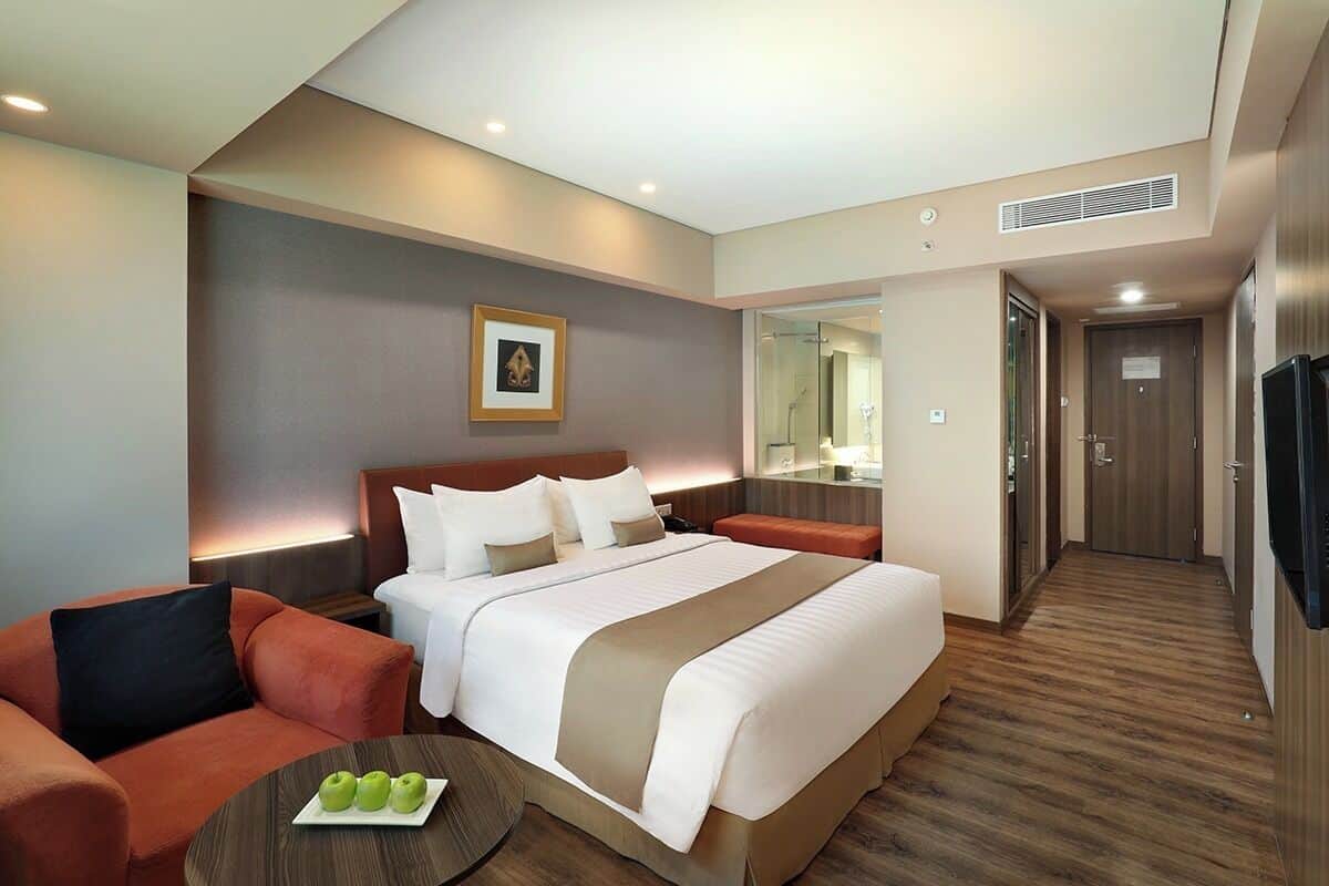 Une chambre d’hôtel avec un grand lit, un canapé, une petite table avec des pommes, un miroir et une télévision.