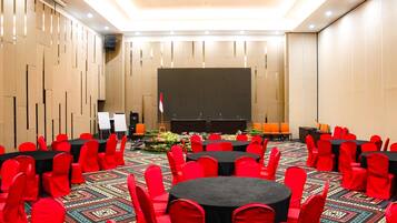A conference room with round tables and red chairs, a stage with a podium, and a projector screen.