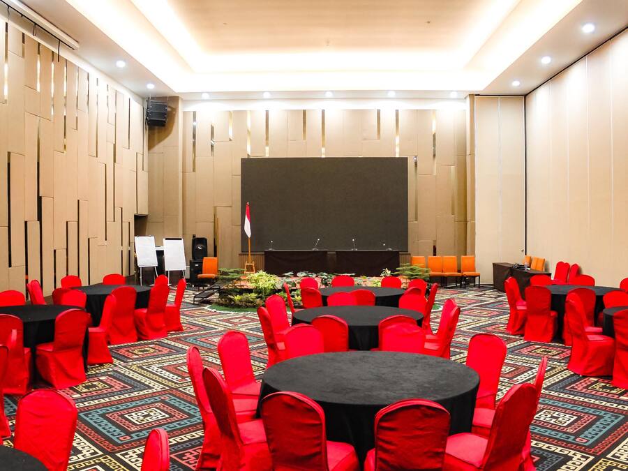A conference room with round tables and red chairs, a stage with a podium, and a projector screen.