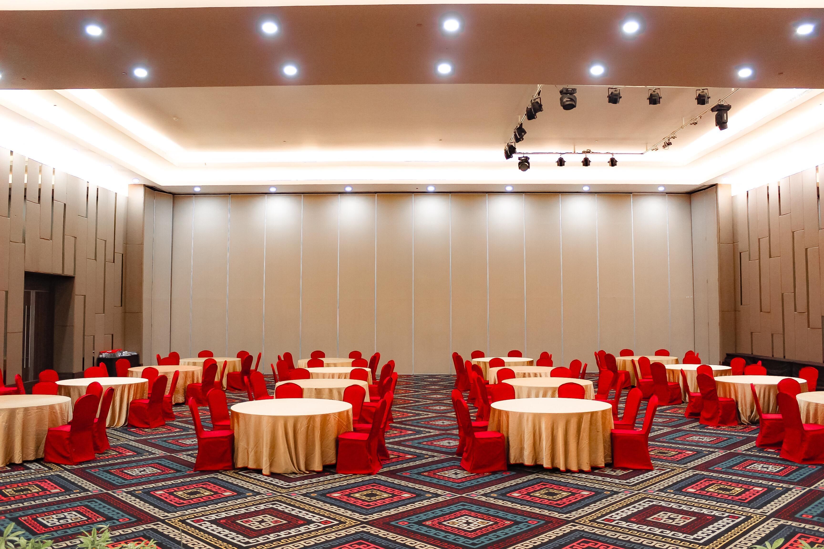 Une salle de conférence avec des tables rondes et des chaises rouges, un sol recouvert de moquette et un éclairage encastré.