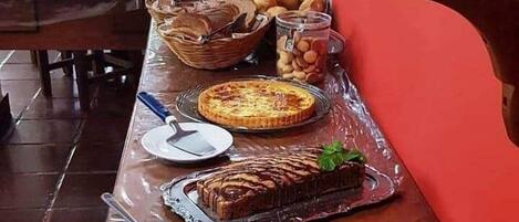 Una mesa de buffet con diversos platos, incluyendo una tarta, un pastel y un postre redondo grande, cubiertos con plástico.