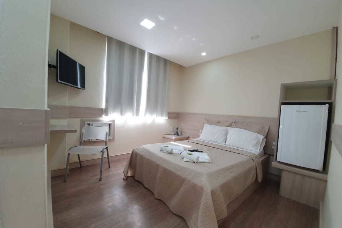 A hotel room with a bed, a chair, a television, and a refrigerator.