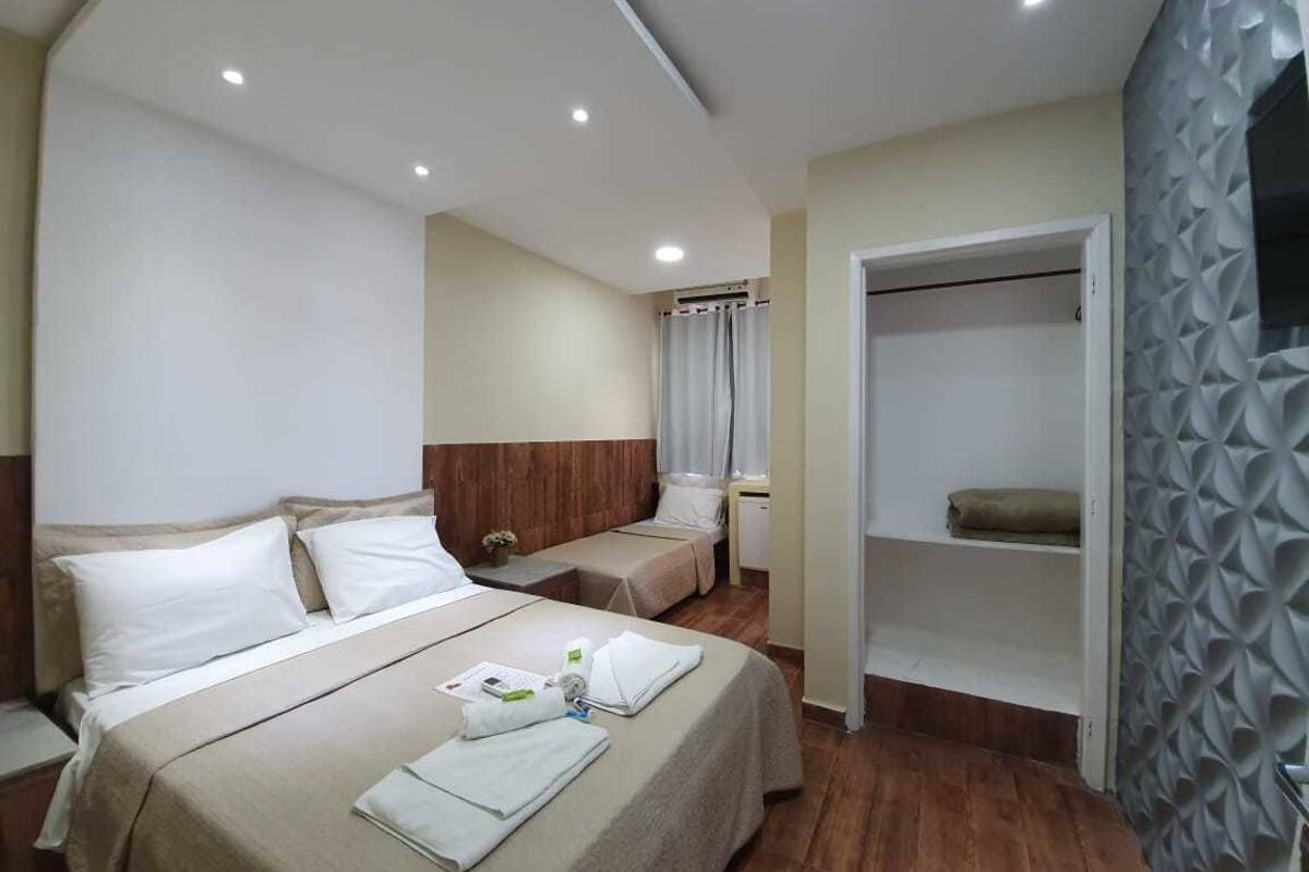 A hotel room with a large bed, a smaller bed, a walk-in closet, and a shower area.