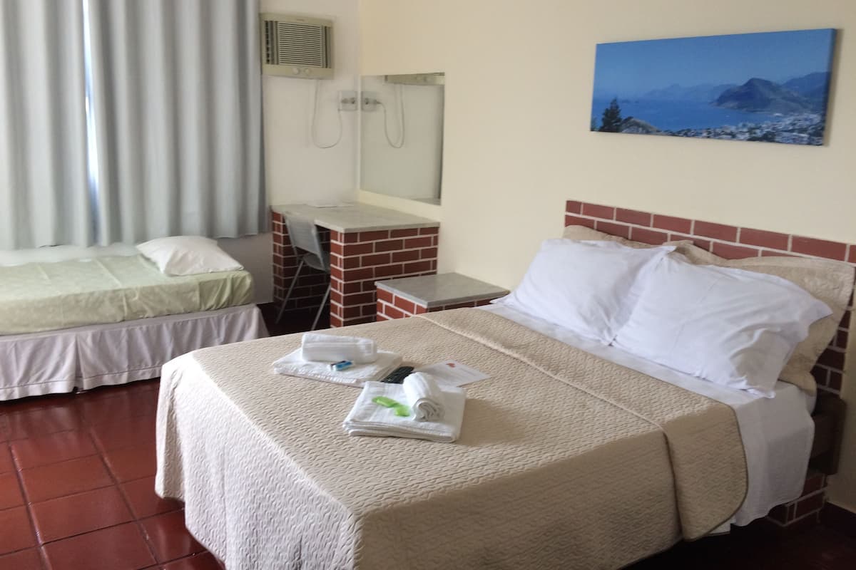 A hotel room with two beds, a desk, a mirror, and a painting of a mountain landscape.