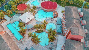 An aerial view of a resort with multiple swimming pools, palm trees, and a large covered area. - Lagoa Quente Hotel (Caldas Novas)