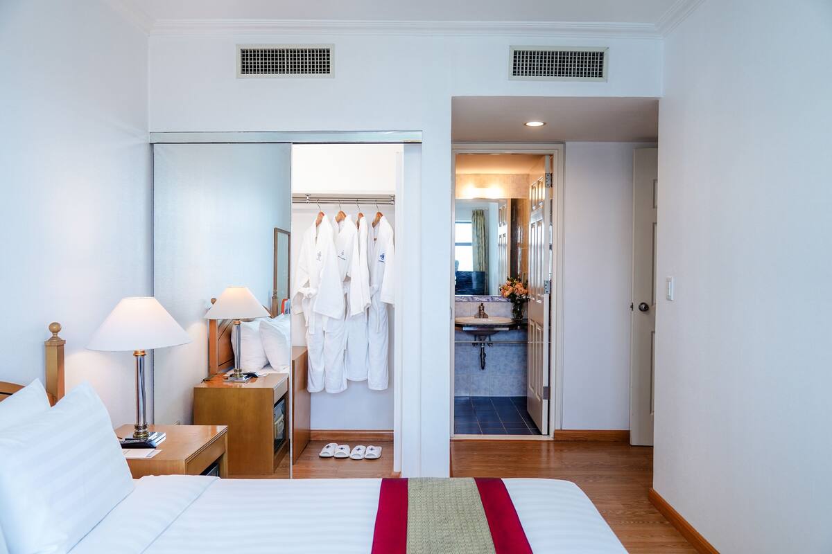 Ein Hotelzimmer mit einem Bett, Nachttischlampen, einem Kleiderschrank und einem durchgegangenen Tür einsehbaren Badezimmer.