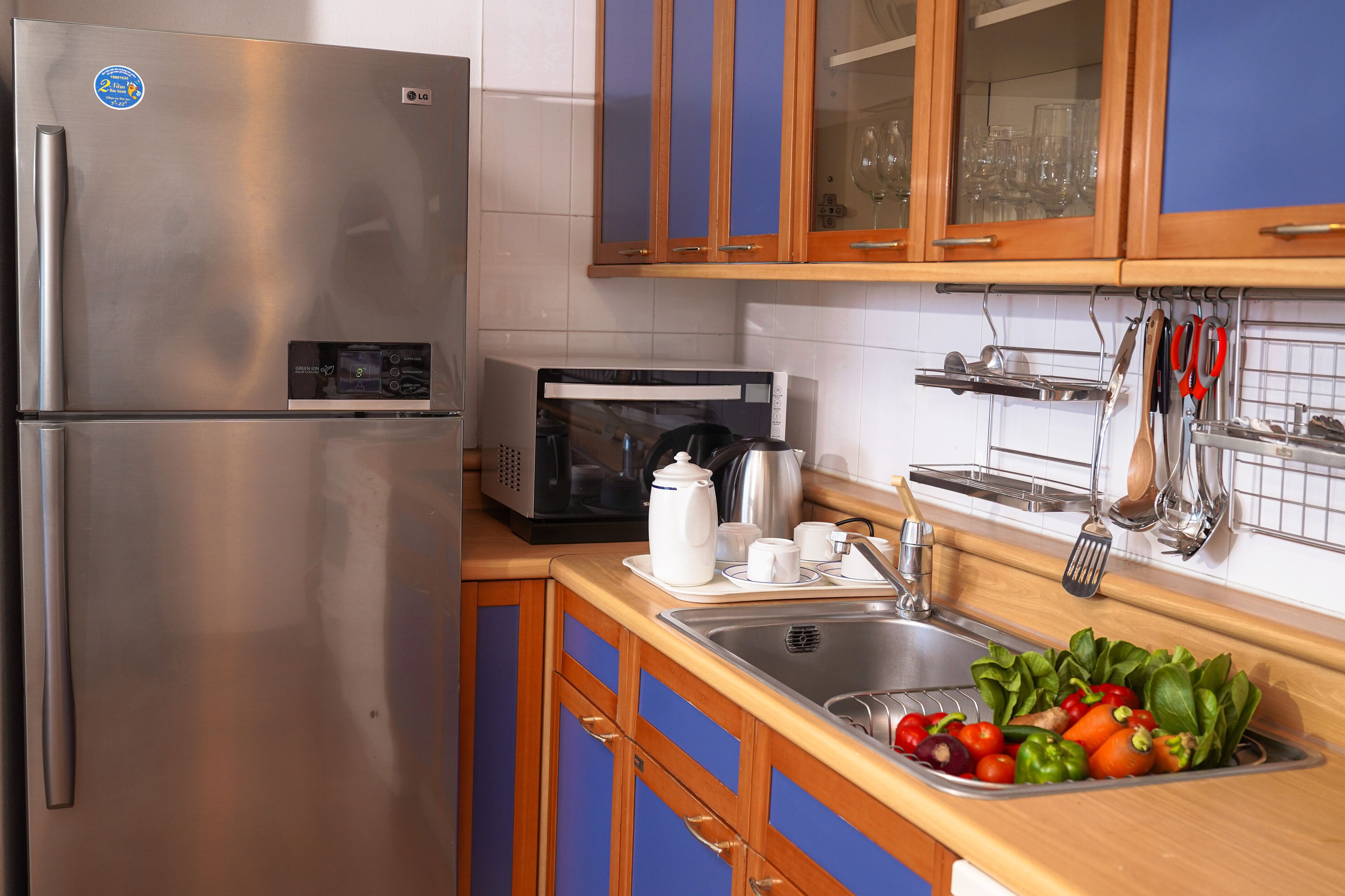 A kitchen with stainless steel appliances, wooden cabinets, and a sink with fresh vegetables.